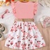 Pink top and floral skirt dress on a wooden surface with shoes and lace in the background.
