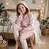 Girl wearing a pink crushed velour hoodie and joggers set sitting in a bedroom.   