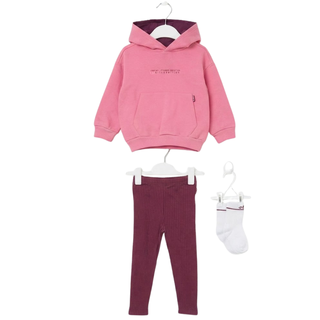 A flat lay of a children's 3-piece outfit consisting of a pink hooded sweatshirt with a small chest print and kangaroo pocket, maroon ribbed leggings, and a pair of white socks with maroon trim, all hanging or arranged on individual white hangers against a plain white background.