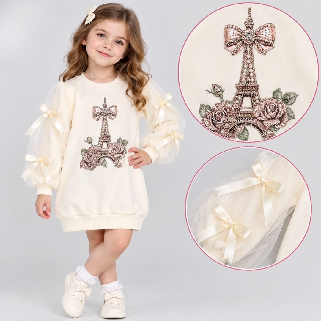 A young girl models a cream-colored long-sleeve dress featuring an embroidered Eiffel Tower and roses on the front, with sheer tulle sleeves decorated with cream satin bows. Two circular inset close-ups on the right show detailed views of the embroidered tower motif and a close-up of the bow on the sleeve.