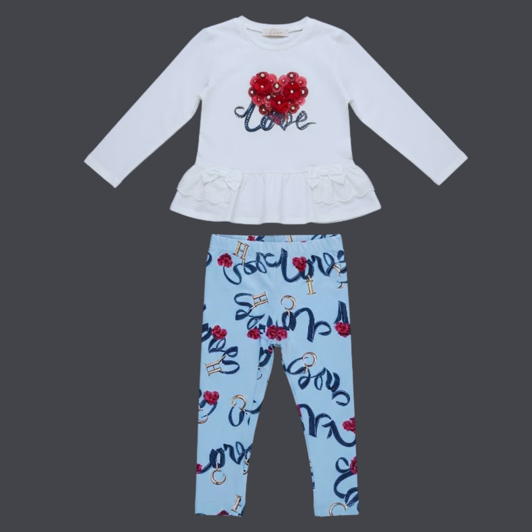 A two-piece children's outfit set featuring a white long-sleeve top with a red heart and 'love' script on the chest, paired with light blue leggings printed with 'love' in navy script, red hearts, and gold keys, displayed on a dark gray background.