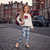 A young girl stands on a cobblestone street in London, wearing a white long-sleeve top with a red glittery heart and the word 'Love' on the front, paired with light blue leggings featuring a red and black script and heart pattern. Red double-decker buses and black cabs are visible in the background.
