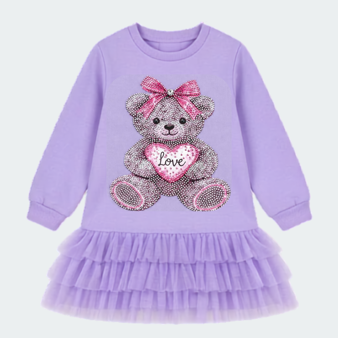 A children's lavender long-sleeve dress with a ruffled tulle skirt and a large rhinestone teddy bear graphic on the front holding a pink heart that says 'Love'.