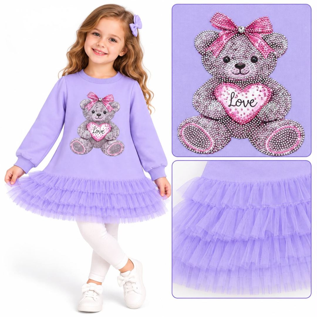 A young girl wearing a lavender long-sleeve dress with a tulle skirt and a rhinestone teddy bear graphic on the front. The dress features a pink bow and a pink heart with the word 'Love' in the center.