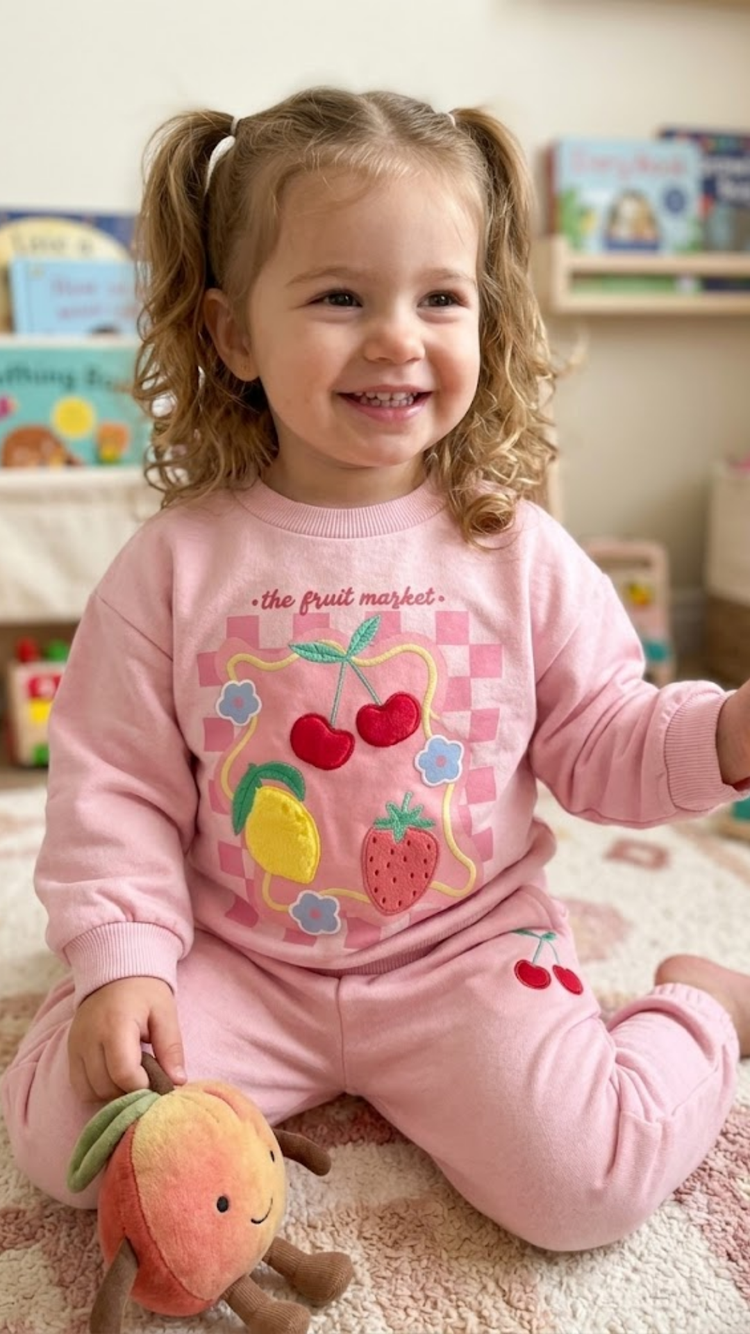 Child wearing a pink outfit with fruit designs in a playroom.