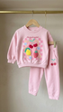 Pink children's sweatshirt and pants set with fruit design on a hanger against a neutral background