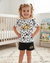 A young girl with curly blonde hair in pigtails stands in a nursery wearing a white short-sleeve t-shirt and black shorts. The t-shirt features black polka dots, cartoon character prints, and gold 'Disney 101 Animal Kingdom' text.
