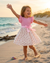 Young girl in a pink dress playing on a sandy beach with ocean in the background