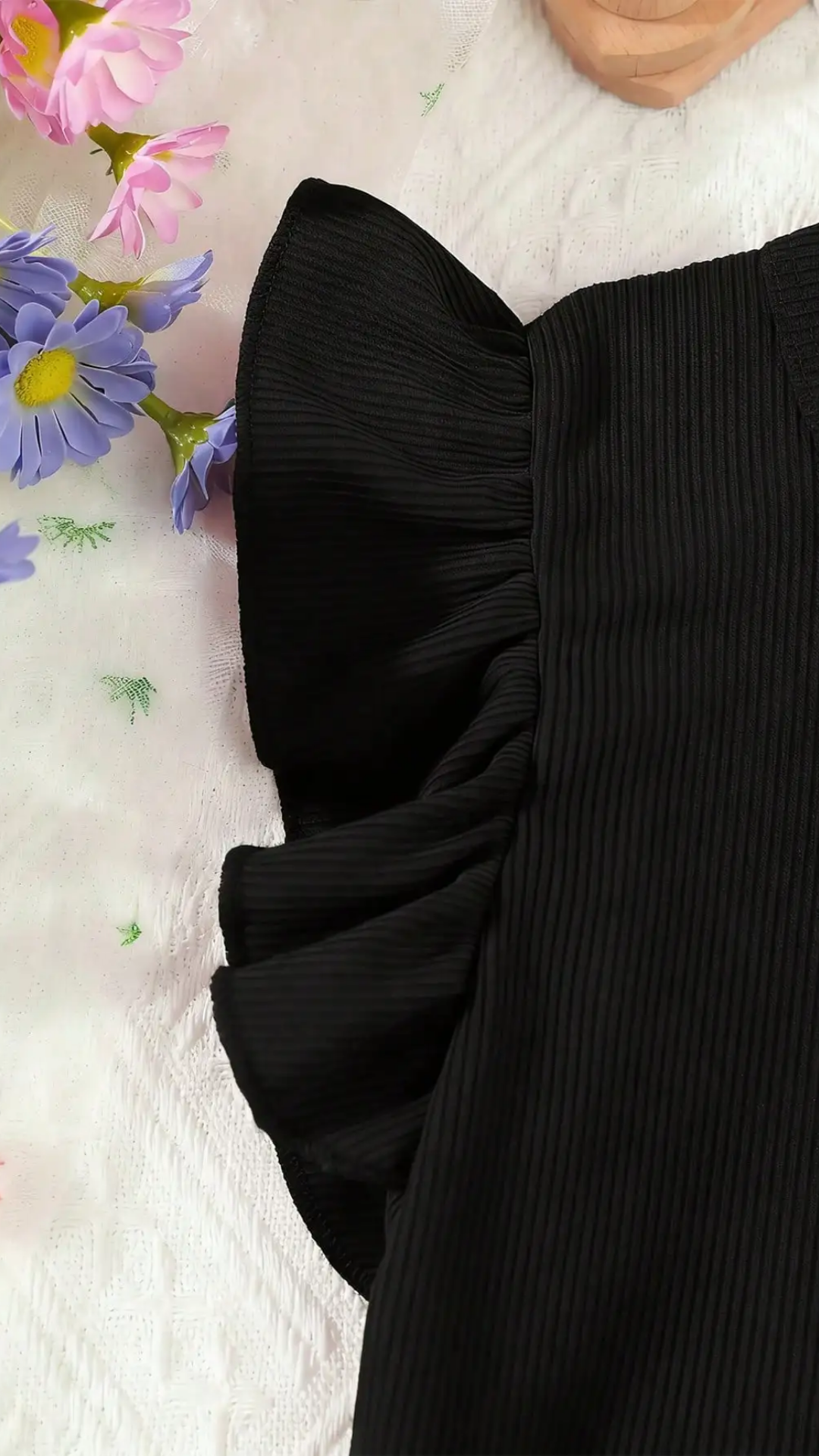 Black ruffled top with flowers in the background