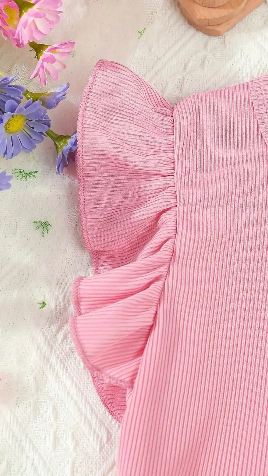 Close-up of a pink ribbed fabric with ruffled edge, surrounded by flowers on a light background
