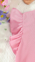 Close-up of a pink ribbed fabric with ruffled edge, surrounded by flowers on a light background