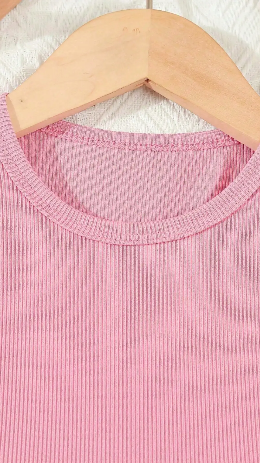 Close-up of a pink ribbed garment on a wooden hanger with a white textured background