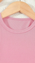 Close-up of a pink ribbed garment on a wooden hanger with a white textured background