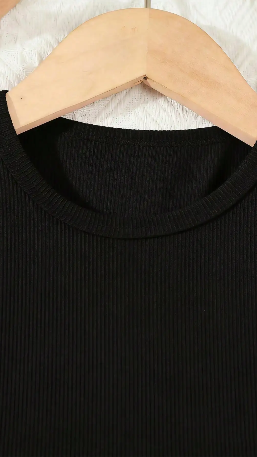 Black sweater on a wooden hanger against a white textured background