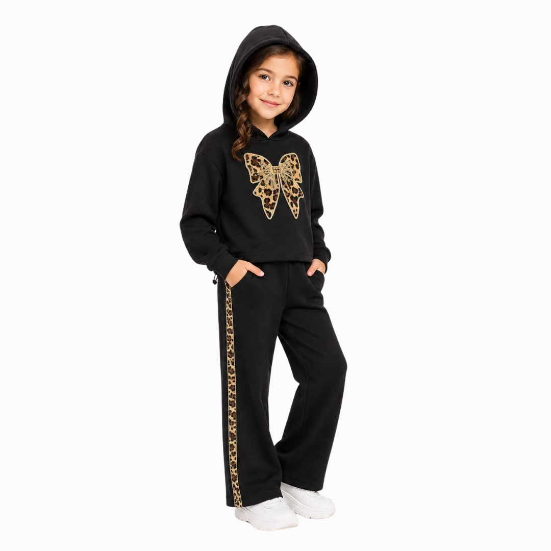 A young girl modeling a black two-piece tracksuit with a gold leopard-print butterfly graphic on the hoodie and a matching gold leopard-print stripe down the pants, set against a plain white background.