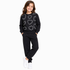 A young girl modeling a black sweatshirt and matching sweatpants set. The sweatshirt features a pattern of glittery silver hearts, and she is wearing white sneakers, set against a plain white background.
