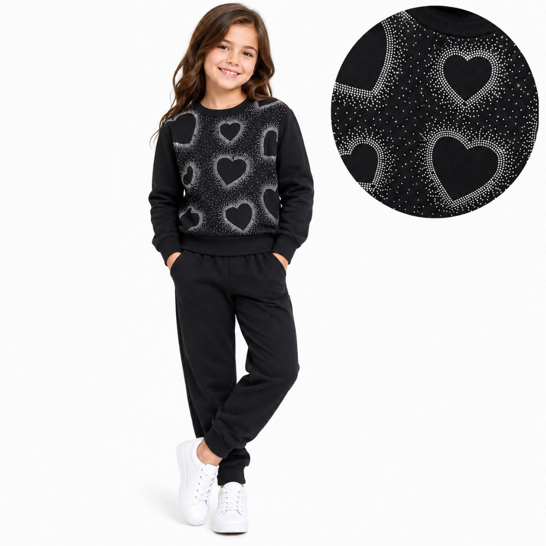 A young girl modeling a black sweatshirt and matching sweatpants set with a glittery heart pattern, shown against a plain white background with a circular detail inset of the heart pattern.