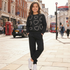 A young girl stands on a London street wearing a black crewneck sweatshirt with a gray heart pattern and matching black sweatpants, paired with white sneakers.