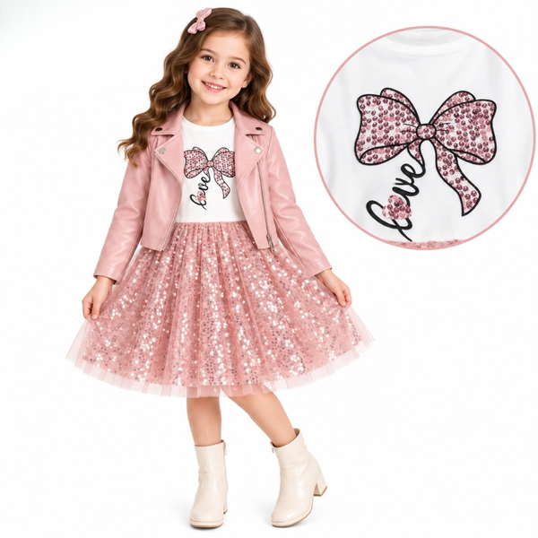 A young girl models a pink sequined tulle skirt with a white graphic tee and a pink faux-leather jacket, shown against a white background with a circular detail inset of the shirt's bow design.