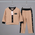 A children's two-piece clothing set displayed on hangers against a gray background, featuring a beige cardigan-style top with black trim and matching beige pants with black side panels.