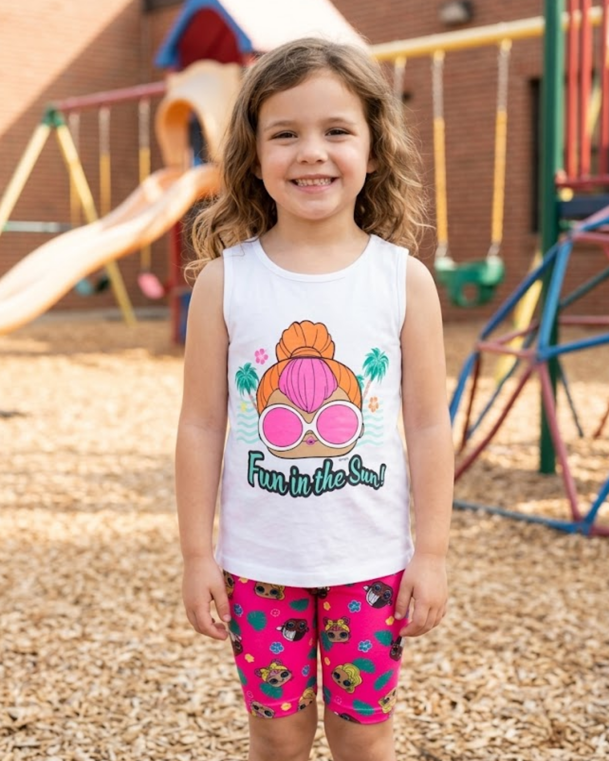 Young girl wearing a sleeveless shirt with a sun design and shorts on a playground.
