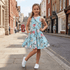 Young girl in a floral dress standing on a city street.