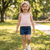 Young girl in a pink top and blue shorts standing in a park.