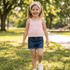 Young girl in a pink top and blue shorts standing in a park.