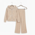 A two-piece children's velour tracksuit in a light beige color, featuring a zip-up hooded jacket and matching wide-leg pants, displayed on hangers against a plain white background.