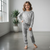 Child wearing a gray pajama set standing in a room with a window and plants.