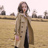 Woman wearing a beige trench coat standing in an open field.