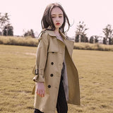 Woman wearing a beige trench coat in an open field