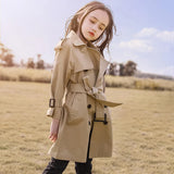 Woman wearing a beige trench coat in an open field with a blue sky.