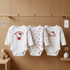 Three baby bodysuits with Hello Kitty designs hanging on a rack against a wooden wall.