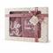 A boxed gift set containing a pink knit sweater and matching blanket. The set is packaged in a cream-colored box with floral patterns, a pink ribbon, and a bow, with the words 'Nook a Lye Body' and 'hello world' visible on the packaging.