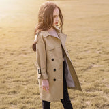 Woman wearing a beige trench coat standing in a field with a warm glow