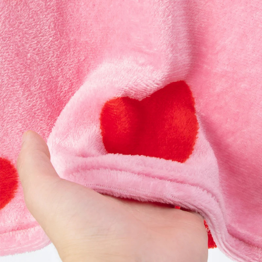 Close-up of pink fabric with red heart shapes held by a hand.
