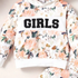 A girls' floral hoodie sweatshirt with a white chest panel featuring the word 'GIRLS' in bold black letters. The hoodie has a watercolor-style print of peach, pink, and white roses with green leaves on a cream background.