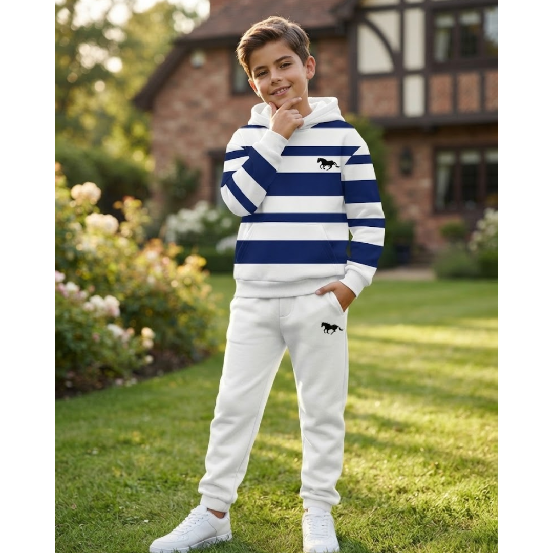 A young boy wearing a matching two-piece tracksuit with navy and white horizontal stripes on the hoodie and solid white sweatpants, standing on a green lawn in front of a house.