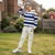 A young boy wearing a navy and white striped hoodie with a small black horse logo on the chest, paired with off-white sweatpants and white sneakers, standing on a grassy lawn in front of a brick house.