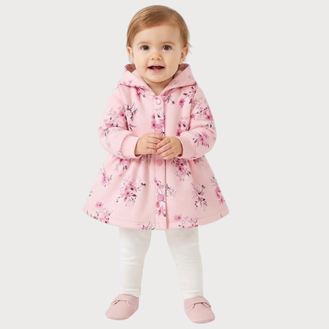 A toddler girl wearing a pink hooded raincoat with a floral print, white leggings, and pink slippers, standing against a light gray background.
