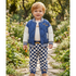 A toddler stands on a garden path wearing a blue quilted bomber jacket with white sleeves, a white shirt, and blue-and-white checkered pants.