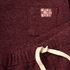 Close-up of a ribbed knit garment in deep burgundy with a cream drawstring and a small chest patch reading 'DAYS like THIS' in pink, burgundy, and dark gray.