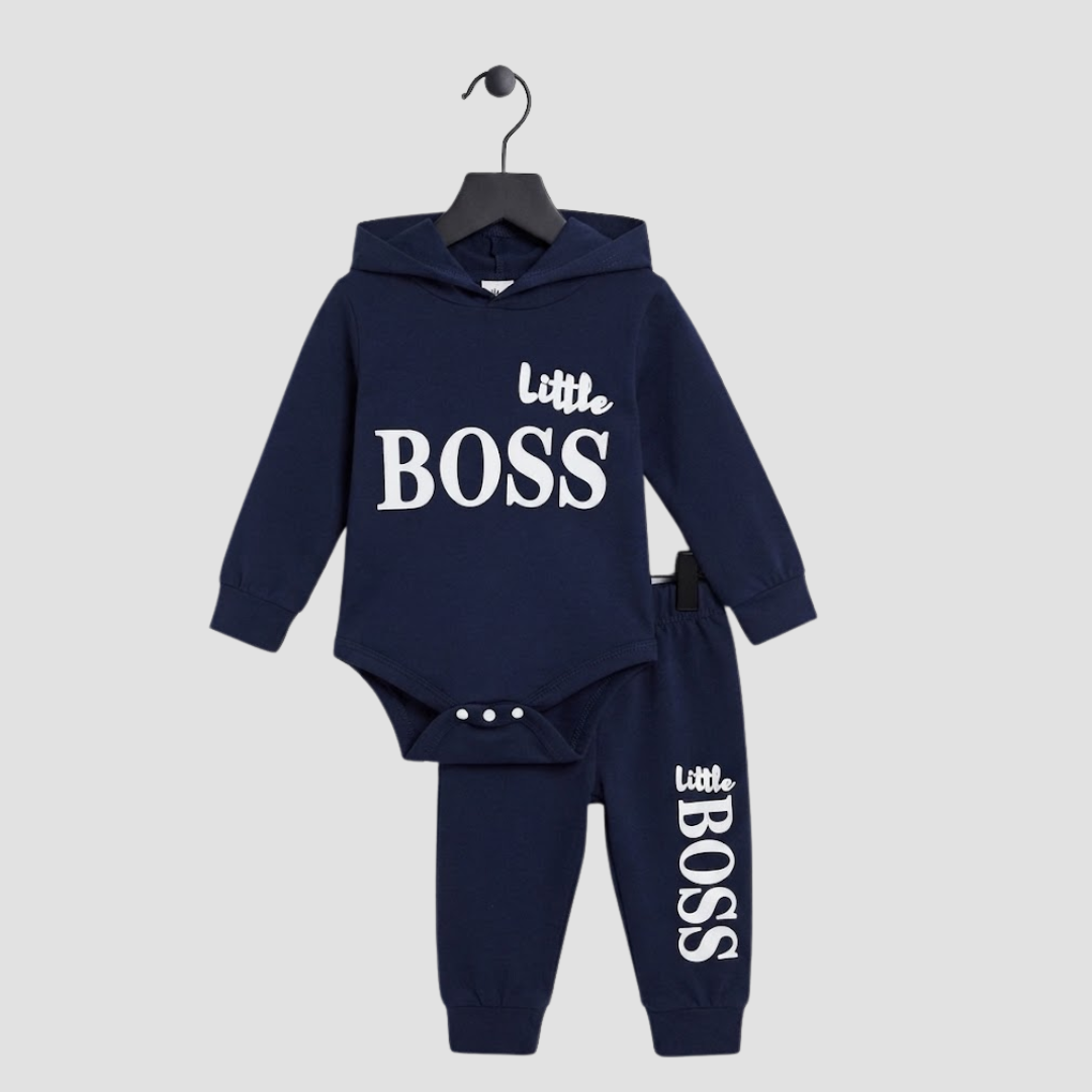 A two-piece baby clothing set from Hugo Boss, featuring a navy blue hooded bodysuit and matching jogger pants, both printed with the brand's 'Little BOSS' logo in white, hanging on a black hanger against a light gray background.