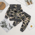 A baby two-piece camouflage outfit laid flat on a white background, featuring a hooded long-sleeve top and matching pants. The camouflage pattern mixes beige, green, black, and gray, with solid dark gray trim on the hood, cuffs, and waistband.