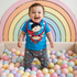 Smiling baby in a Superman outfit standing in a colorful ball pit.