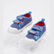 A pair of children's blue canvas sneakers with white rubber soles, featuring colorful cartoon character patches on the velcro straps and a red interior lining, displayed on clear acrylic stands against a white background.
