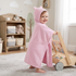 Smiling baby wearing a pink Peppa Pig hooded towel with 3D ears while holding onto a wooden push walker in a nursery.