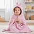 Young toddler smiling while sitting on a rug wrapped securely in a pink Peppa Pig hooded towel with 3D ears.
