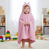 Smiling toddler standing upright in a playroom wrapped in a pink Peppa Pig hooded towel with 3D ears, surrounded by toys.